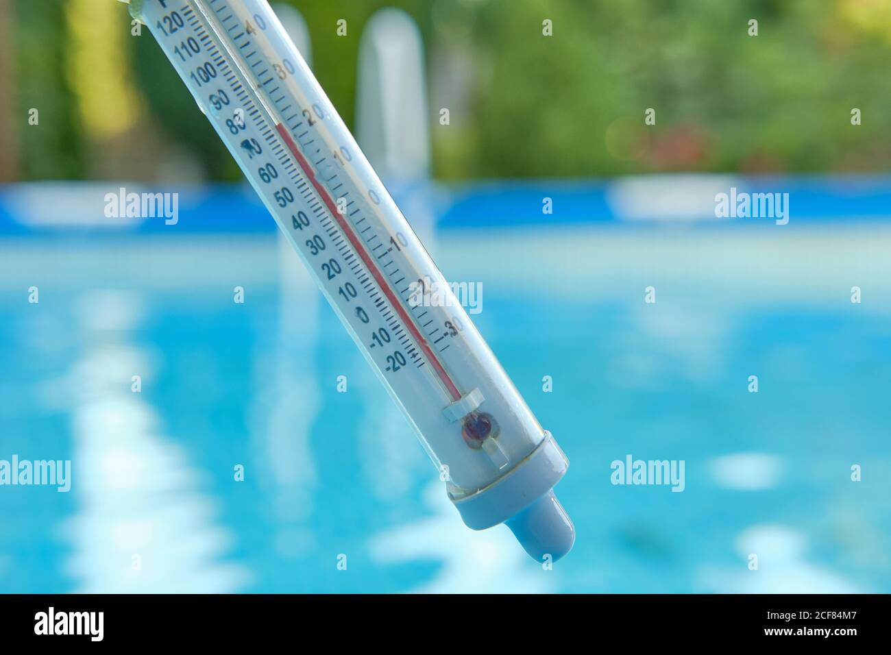 Thermometer measuring water temperature for swimming on a blurred background of blue water in the pool. Summer concept. Stock Photo