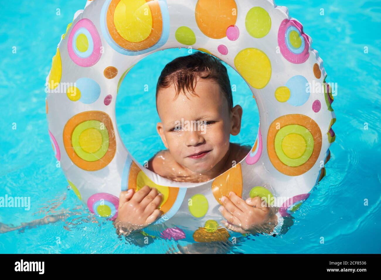 Happy kid with swim ring playing in blue water of swimming pool. Little