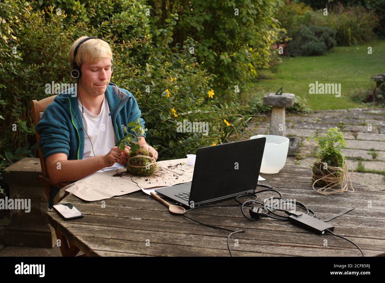Millennial generation young man sitting outside with computer making plant hanging basket Stock Photo
