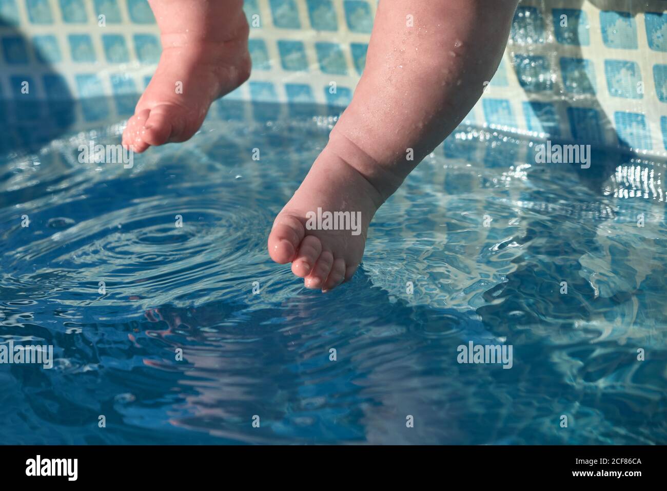 Baby's feet touch the blue water in the pool. Concept of newborn swimming training. Stock Photo