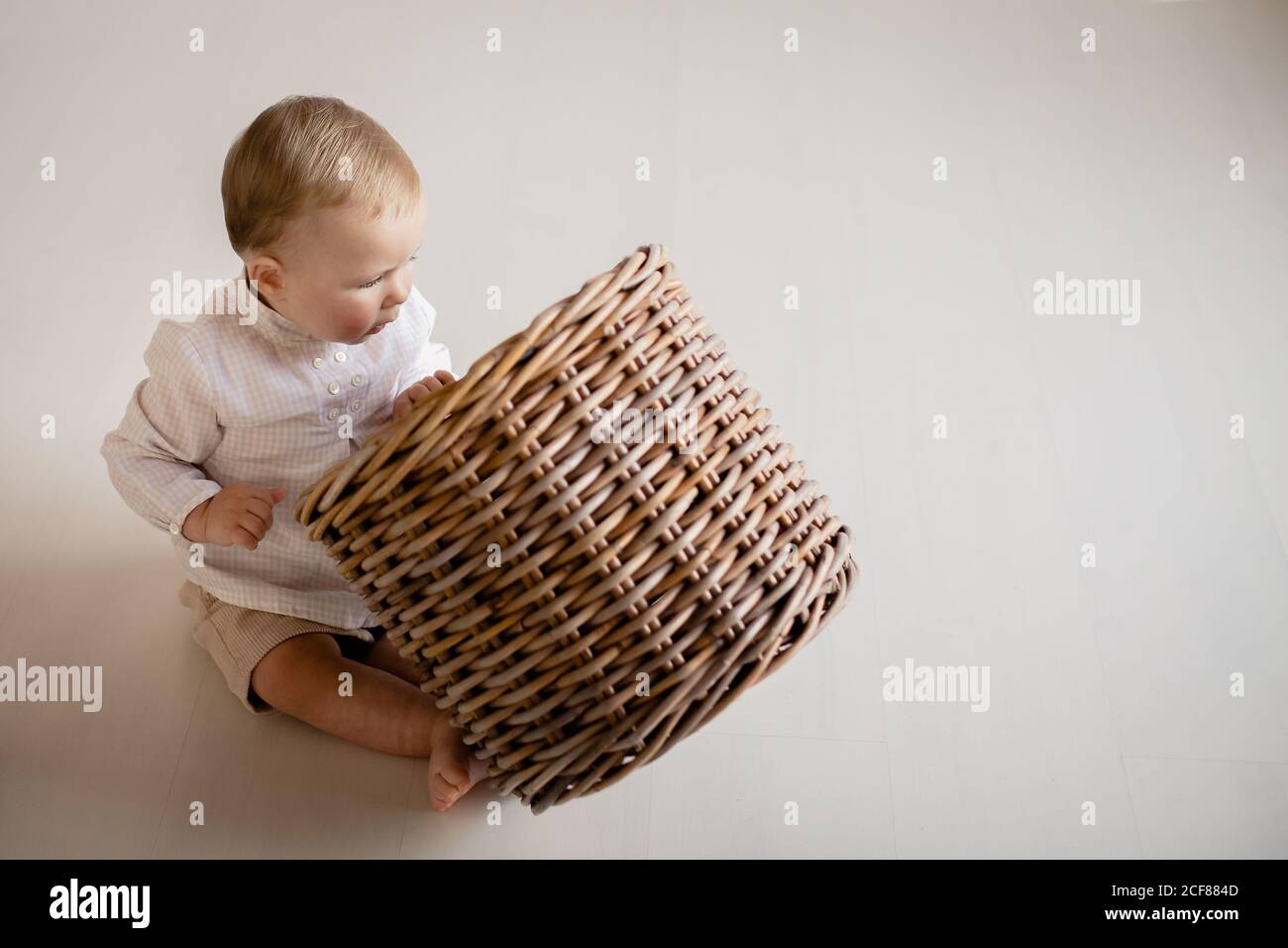 Curious little kid in casual wear sitting barefoot on floor at home and taking plush toys from wicker basket Stock Photo