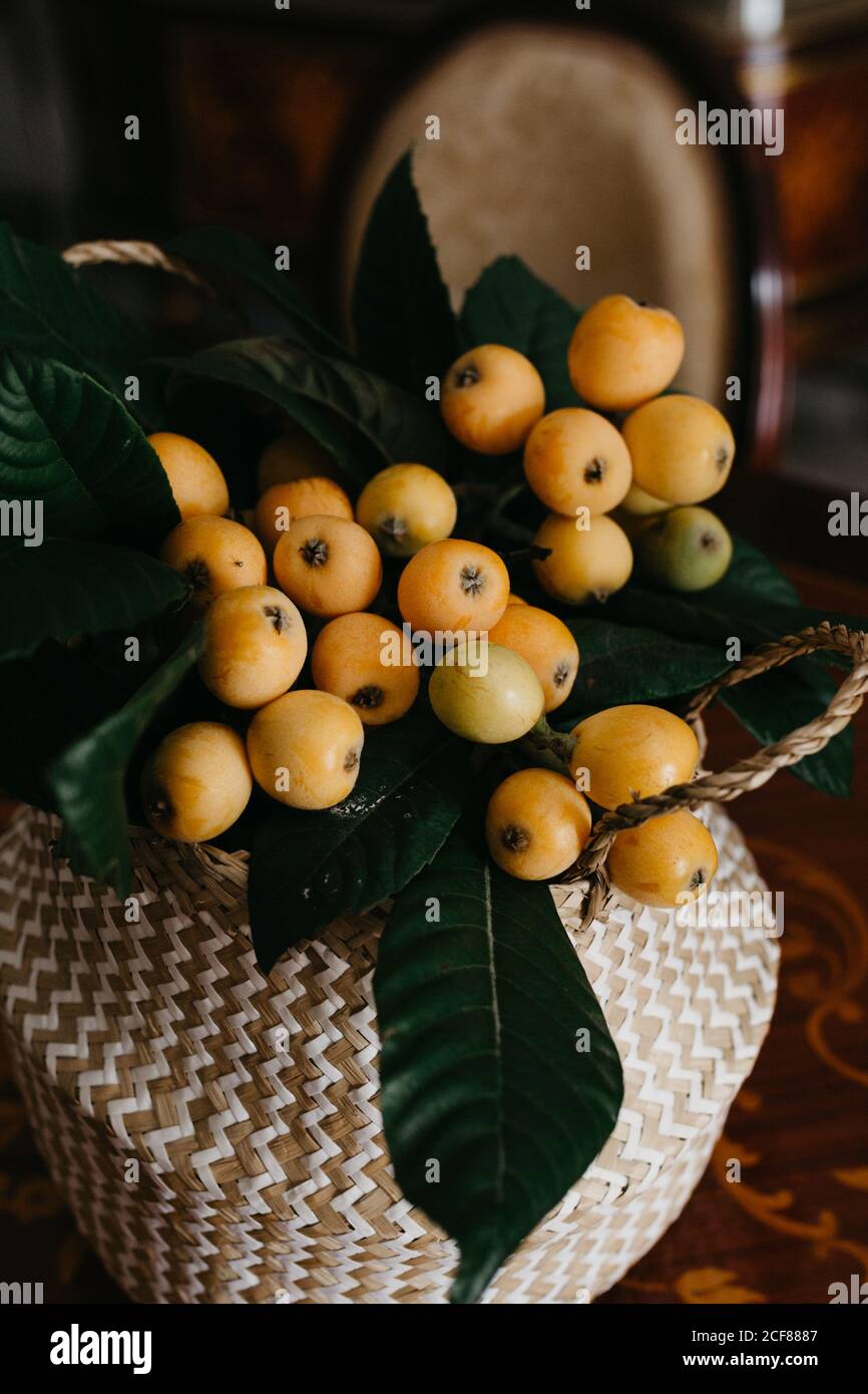 Wicker basket with loquat fruits and green leaves placed on wooden table in vintage styled fashioned interior of retro dining room Stock Photo