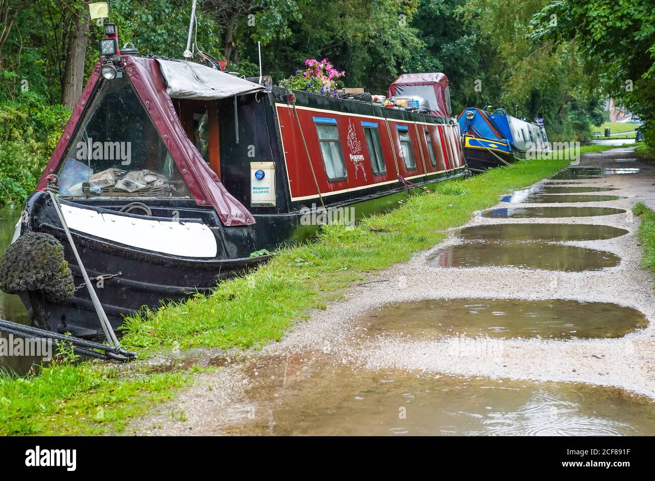 Narrowboats moored alongside UK canal towpath with lots of puddles after heavy rain. Stock Photo