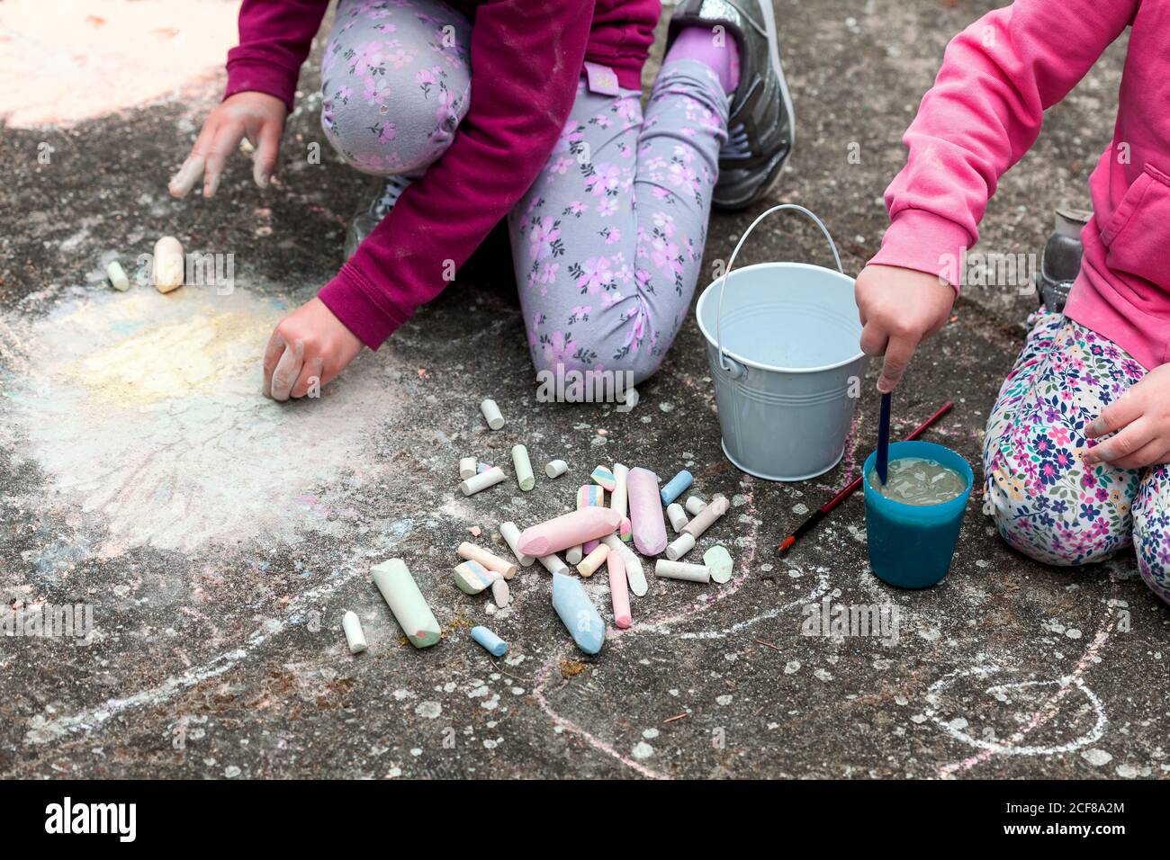 Children drawing with chalk on the concrete sitting on the ground. Art therapy, CBT, simple creativity excercises. Girls drawing with colorful chalk Stock Photo