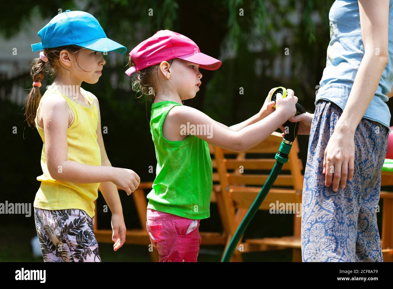 Curious children with their mother examining a turned off water hose in the garden Summer family activities, togetherness, girls enjoying weather Stock Photo