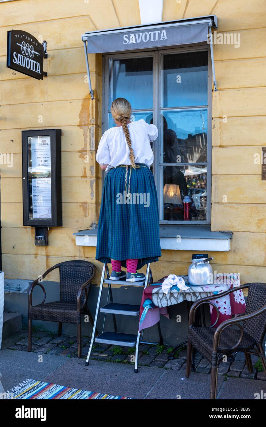 Woman with plait on stepladder cleaning Savotta restaurant window in Kruununhaka district of Helsinki, Finland Stock Photo