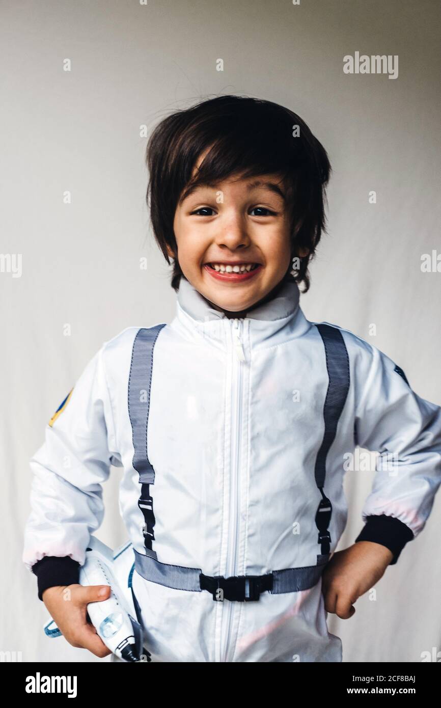 Positive child wearing spaceman uniform standing with toy spaceship and cheerfully smiling at camera Stock Photo