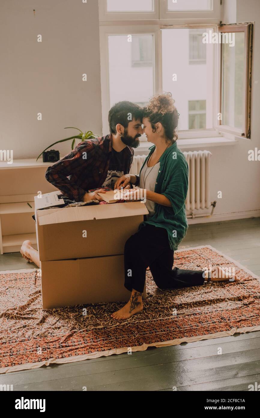 Cheerful couple laughing while sitting next to opened cardboard box in ...