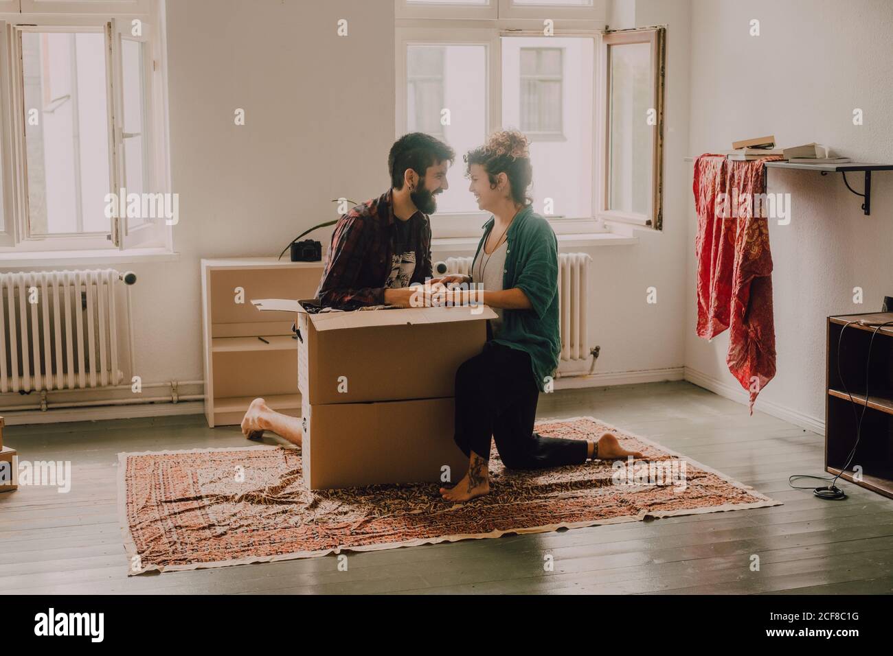 Cheerful couple laughing while sitting next to opened cardboard box in ...