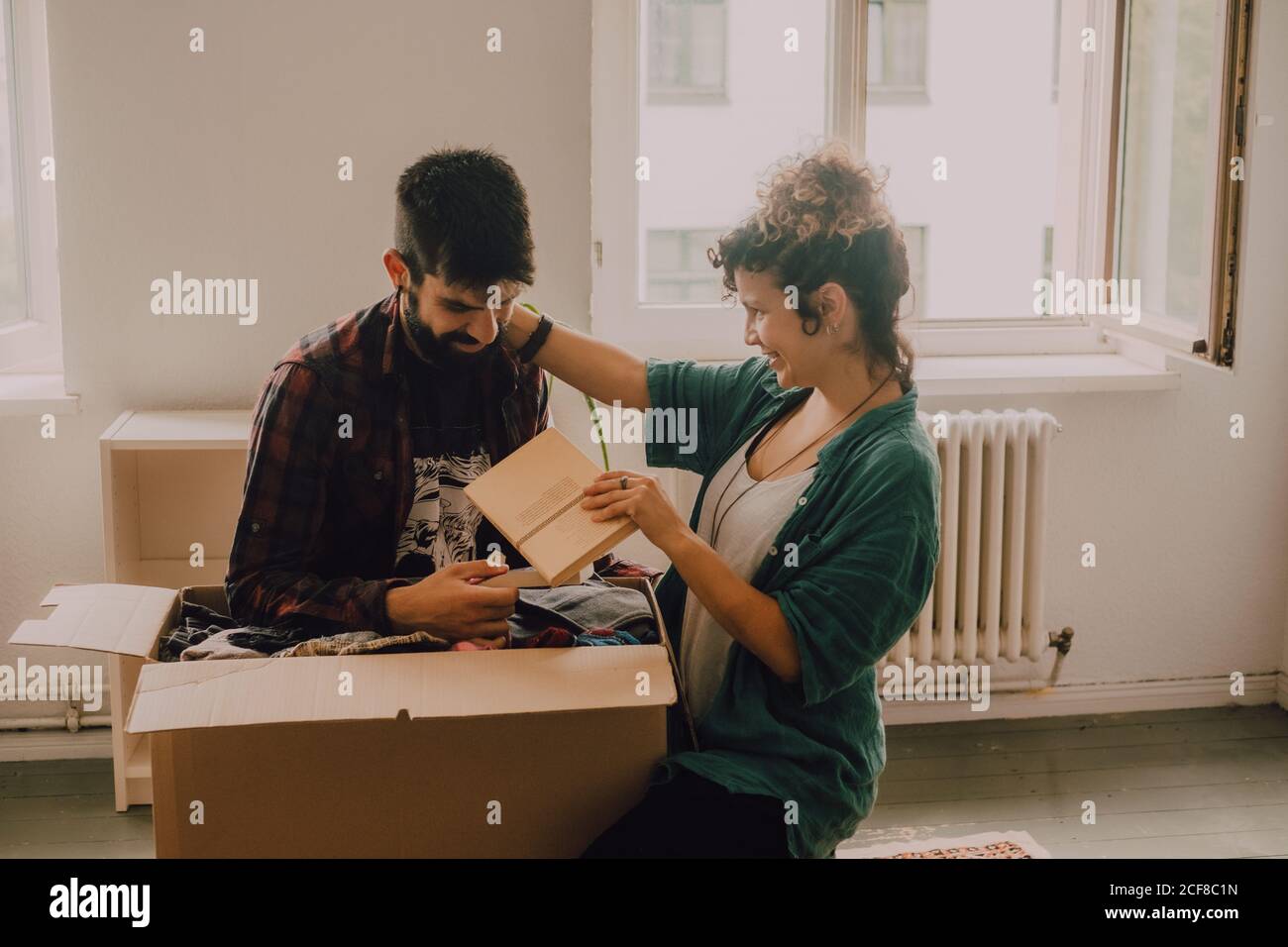 Cheerful couple laughing while sitting next to opened cardboard box in ...