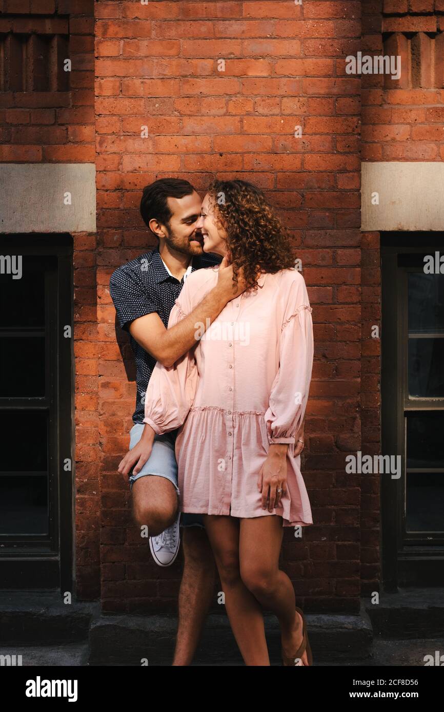 Loving couple cuddling and kissing while standing near brick building in city on sunny day in New York Stock Photo