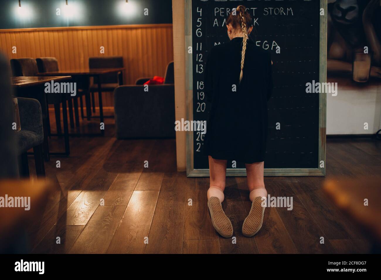 Young woman writing cafe menu on black desk chalkboard using chalk. Stock Photo