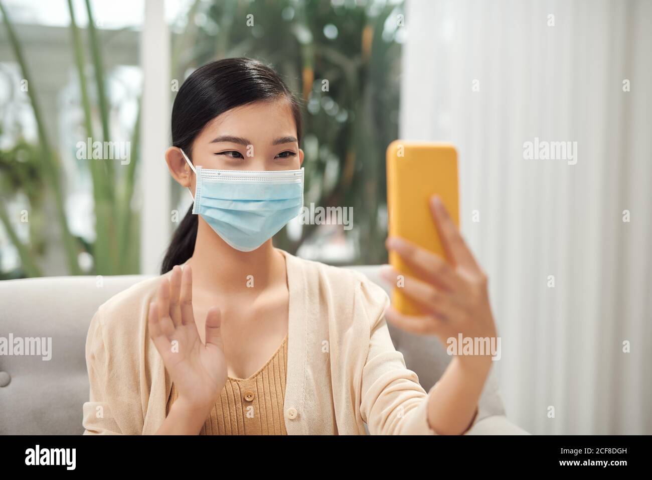 Young woman is talking by videocall in mask. Working from home, talking with friends, taking selfie in mask Stock Photo