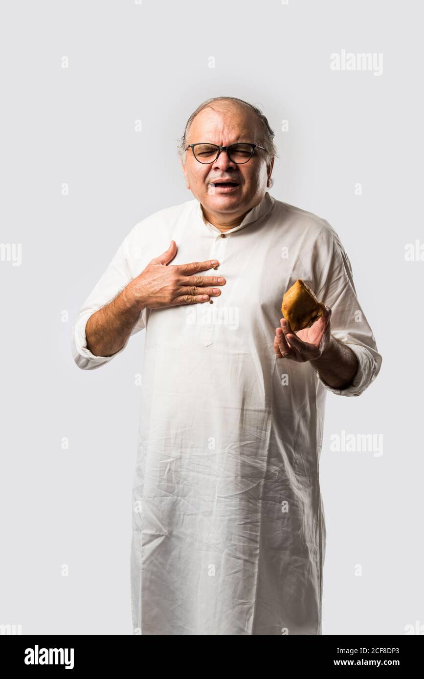 Indian old man or senior man eating samosa or veg pastry Stock Photo