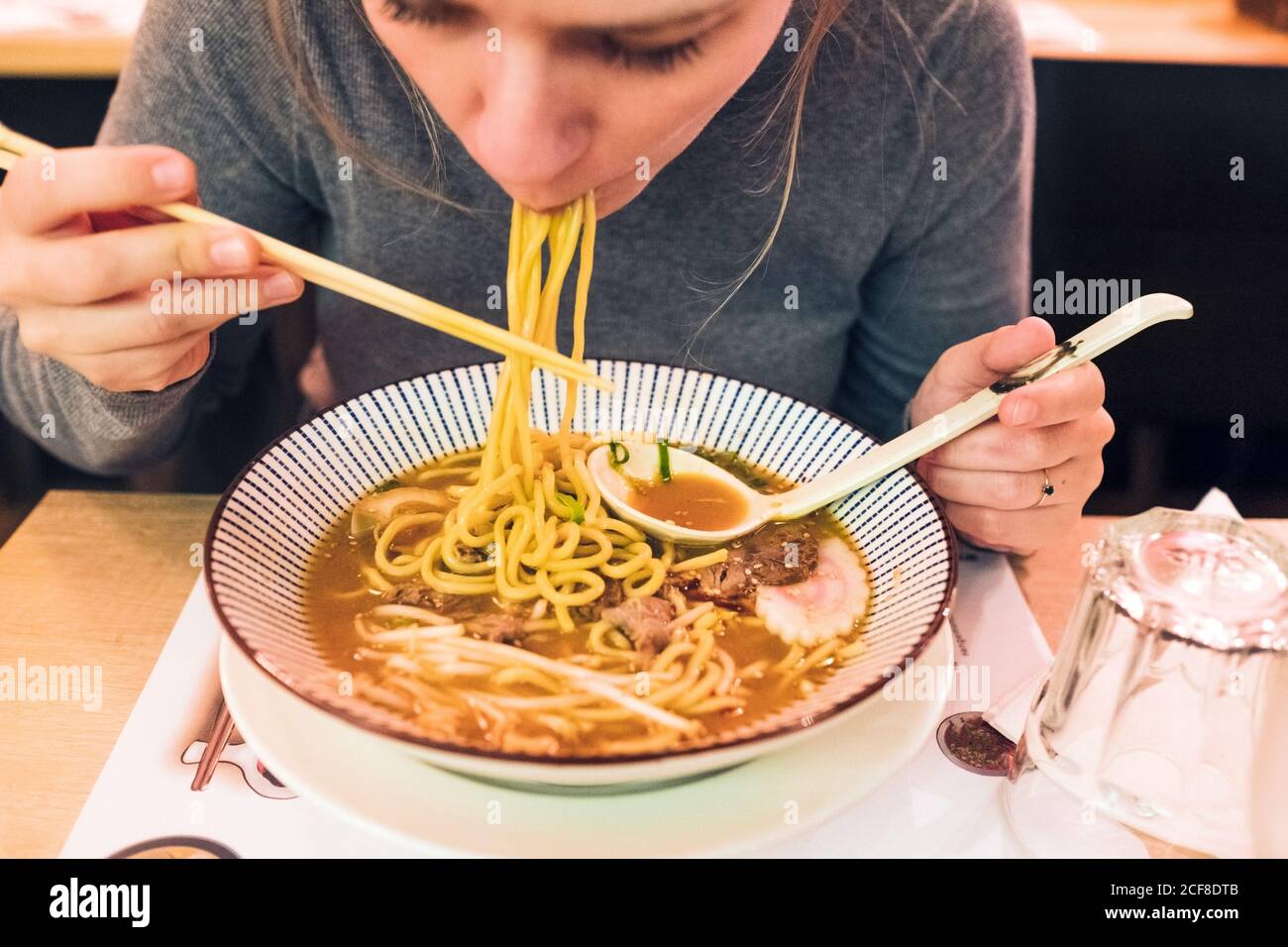 Young female using chopsticks and spoon to eat tasty ramen while sitting at  table in Japanese restaurant Stock Photo - Alamy