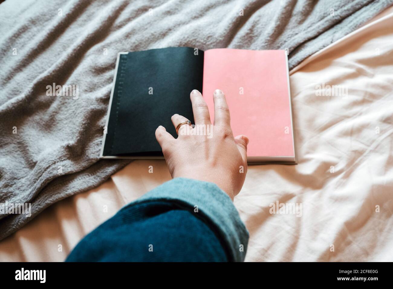 From above faceless female in casual clothes taking opened notebook with empty black and pink pages from soft bed in light modern bedroom Stock Photo