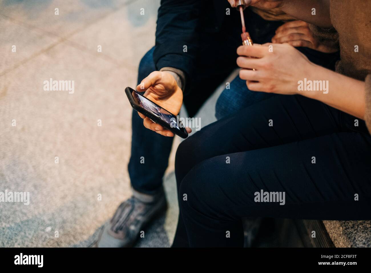 Young man sharing interesting video on smartphone with girlfriend while  sitting on bench on city street together Stock Photo - Alamy