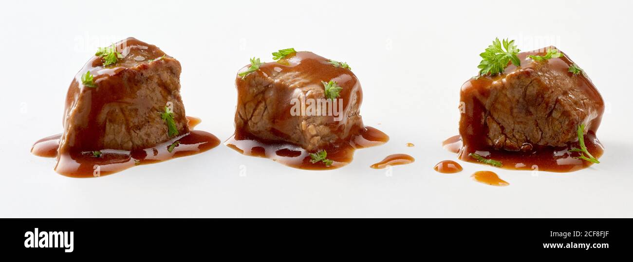 Three diced cubes of beef goulash and gravy arranged individually and garnished with parsley isolated on white Stock Photo