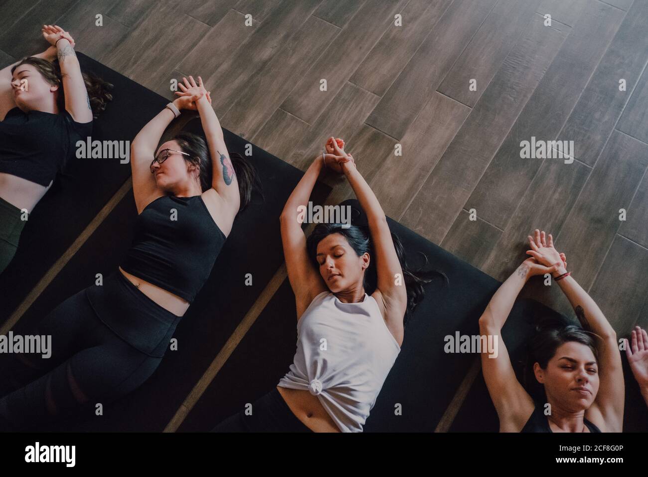 High angle of group of young sporty women and men in sportswear with eyes closed and legs crossed relaxing and deep breathing while lying in savasana position and meditating on sports mats in modern yoga studio Stock Photo