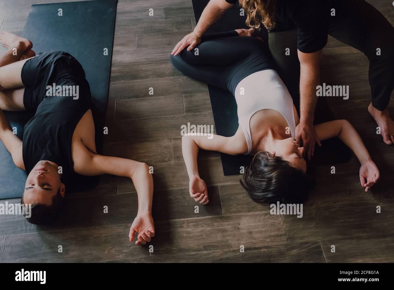 High angle of group of young sporty women and men in sportswear with eyes closed and legs crossed relaxing and deep breathing while lying in savasana position and meditating on sports mats in modern yoga studio Stock Photo
