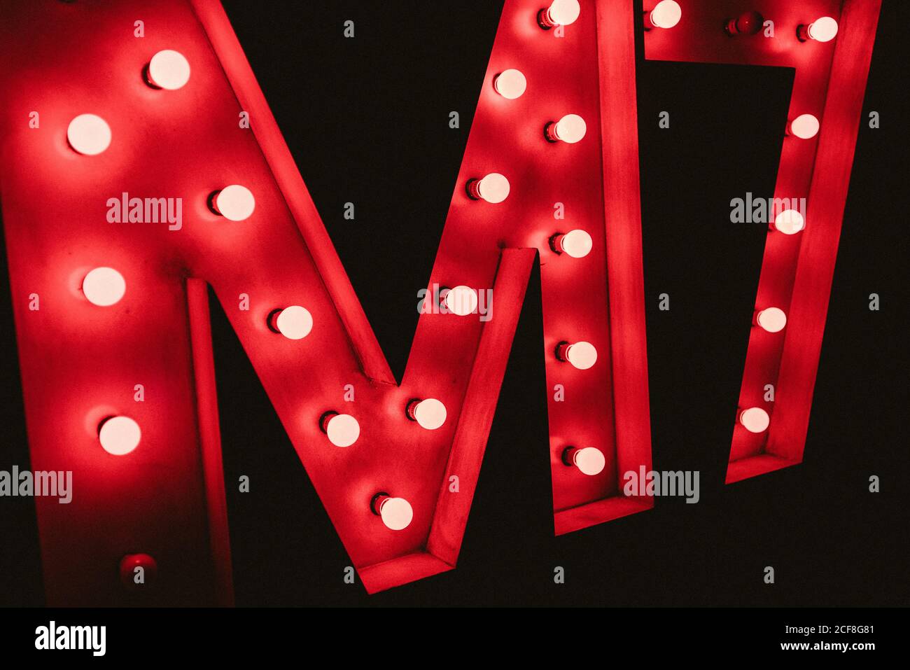 Huge M letter with red neon glowing bulbs on black wall in dark Stock Photo