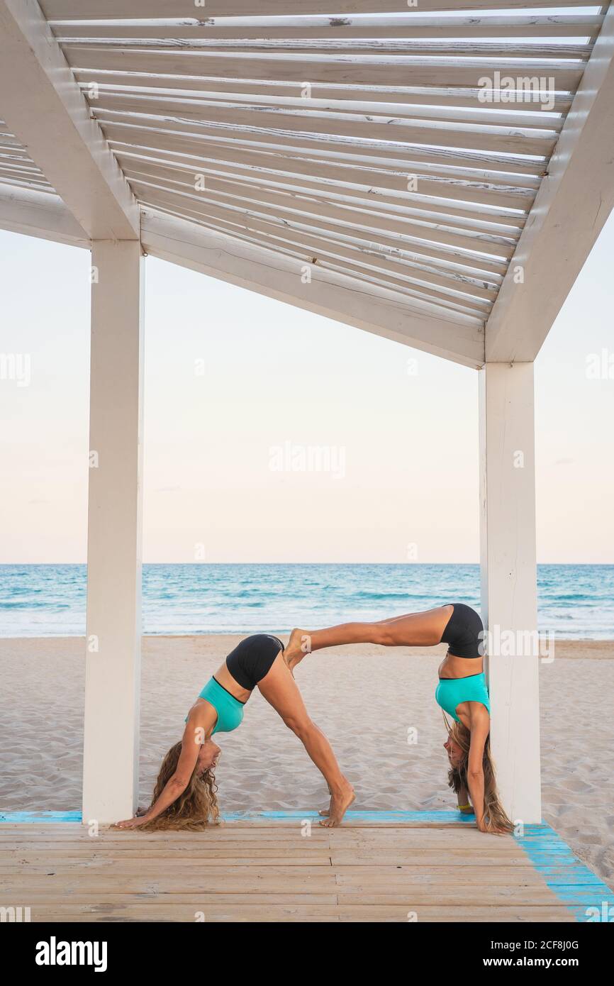 Sportive women making acroyoga posture double dog down on sandy beach Stock Photo