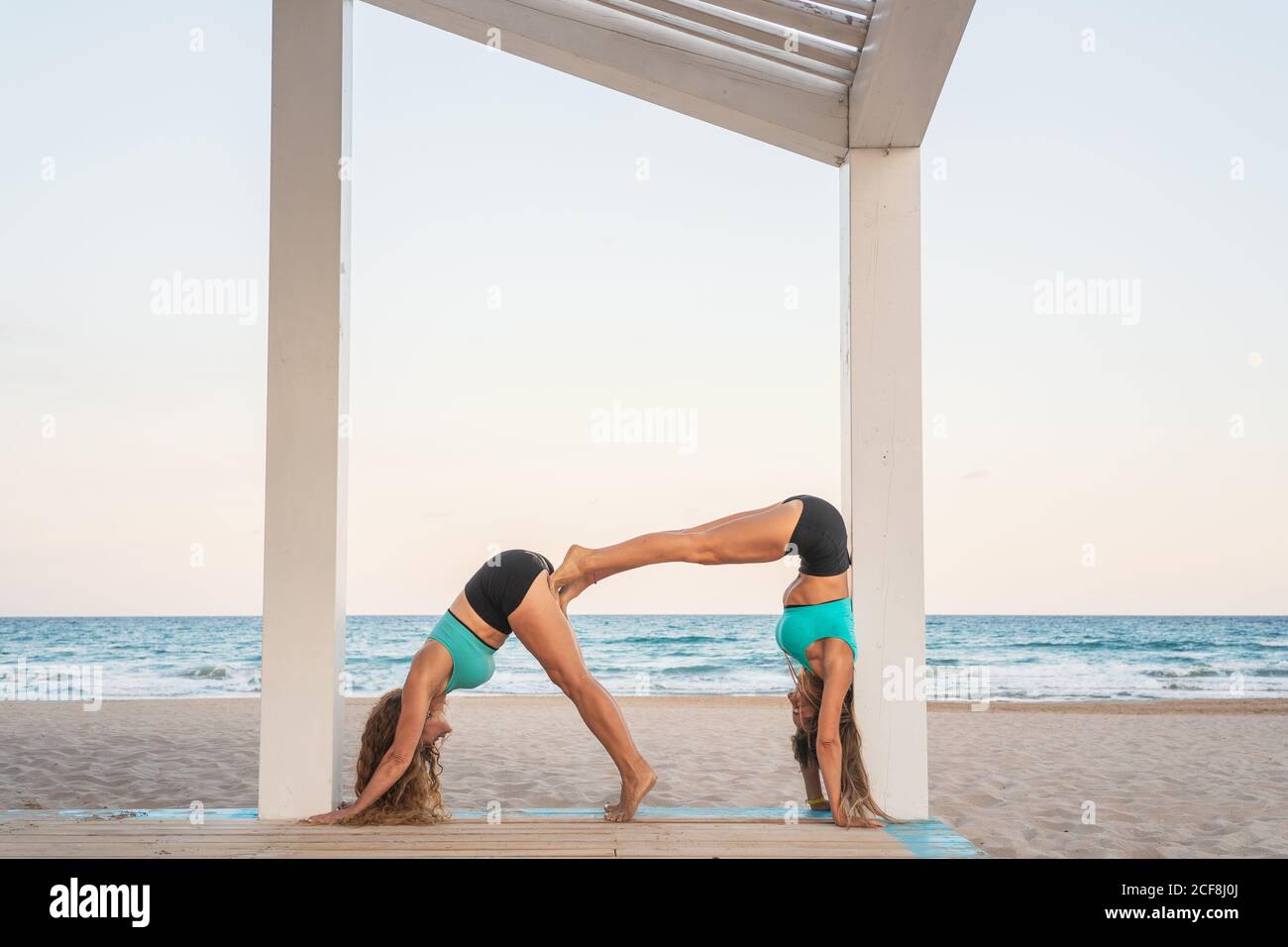 Sportive women making acroyoga posture double dog down on sandy beach Stock Photo