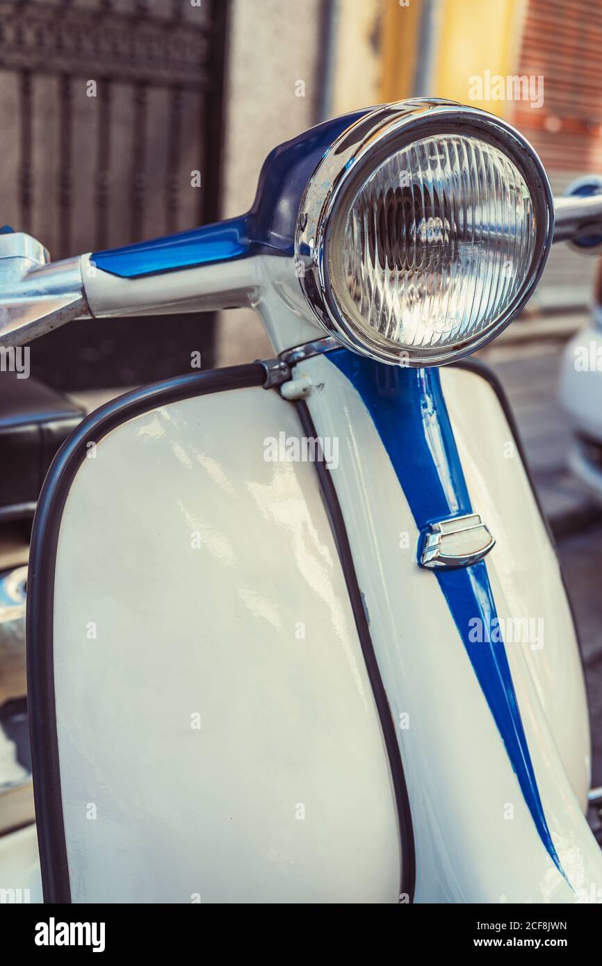 White and blue retro motor scooter with round headlight parked on city street Stock Photo