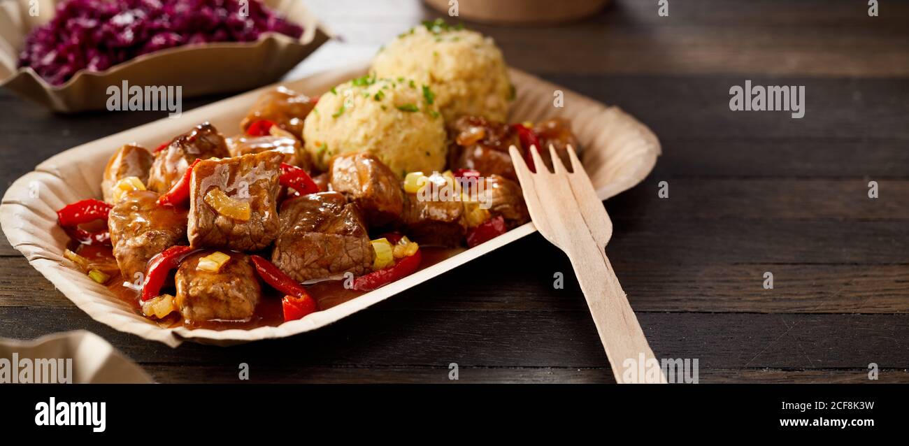 Takeaway serving of spicy chili beef goulash and dumpling on a disposable plate with wooden fork at an event Stock Photo