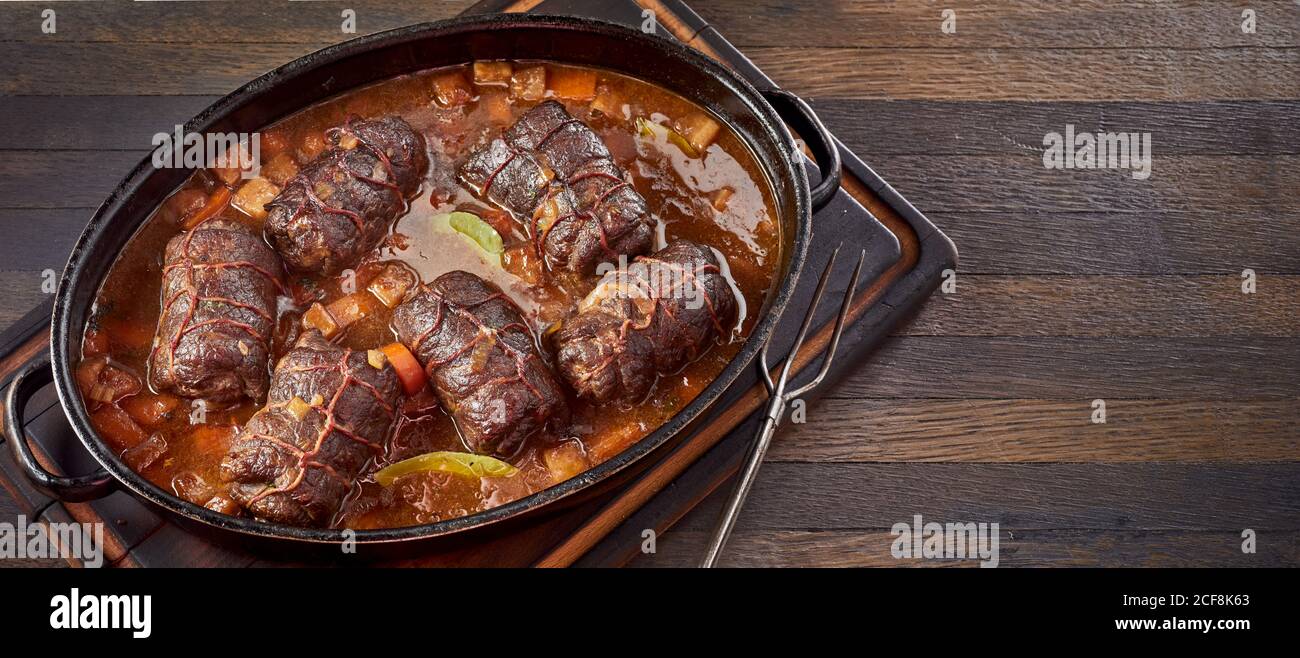 Delicious beef roulades in a piquant gravy seasoned with chili and bay leaves with fresh vegetables viewed high angle on wood with copyspace in a pano Stock Photo