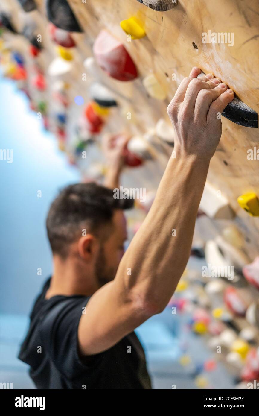 Side view of blurred anonymous strong male athlete in sportswear climbing on colorful wall during workout in modern guy Stock Photo