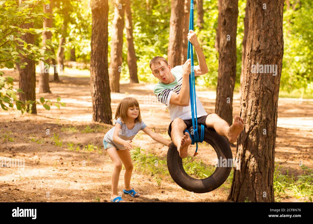 Happy child daughter pushing father on tire swing in autumn garden Stock Photo