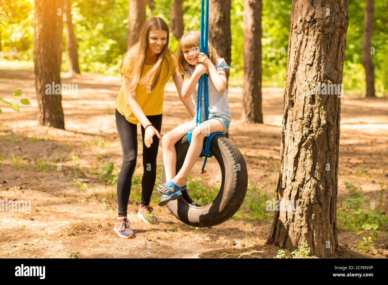 Young mother pushing child daughter on tire swing in autumn park Stock Photo