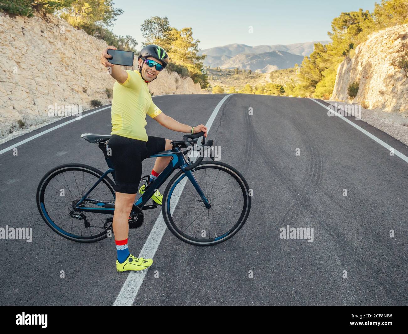 healthy man resting and taking selfie with smartphone while riding a bicycle on a mountain road in a sunny day Stock Photo