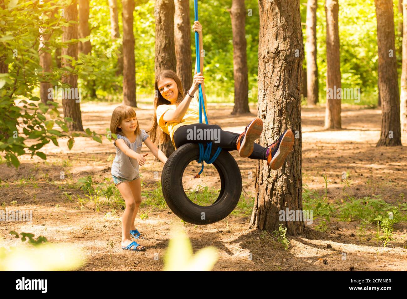 Happy child daughter pushing mother on tire swing in autumn garden Stock Photo