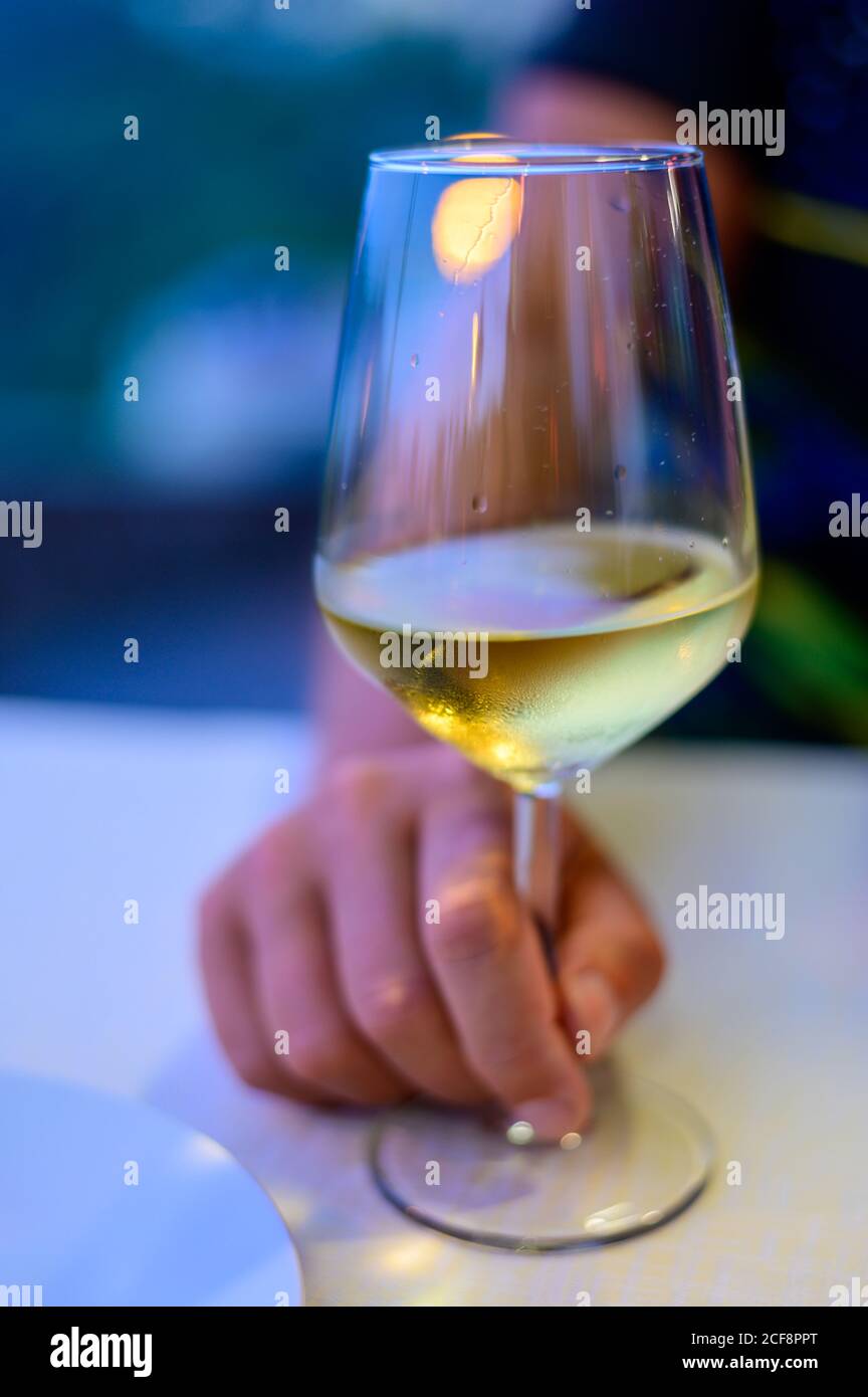 Hand with glass of cold dry white wine served outdoor in cafe at night