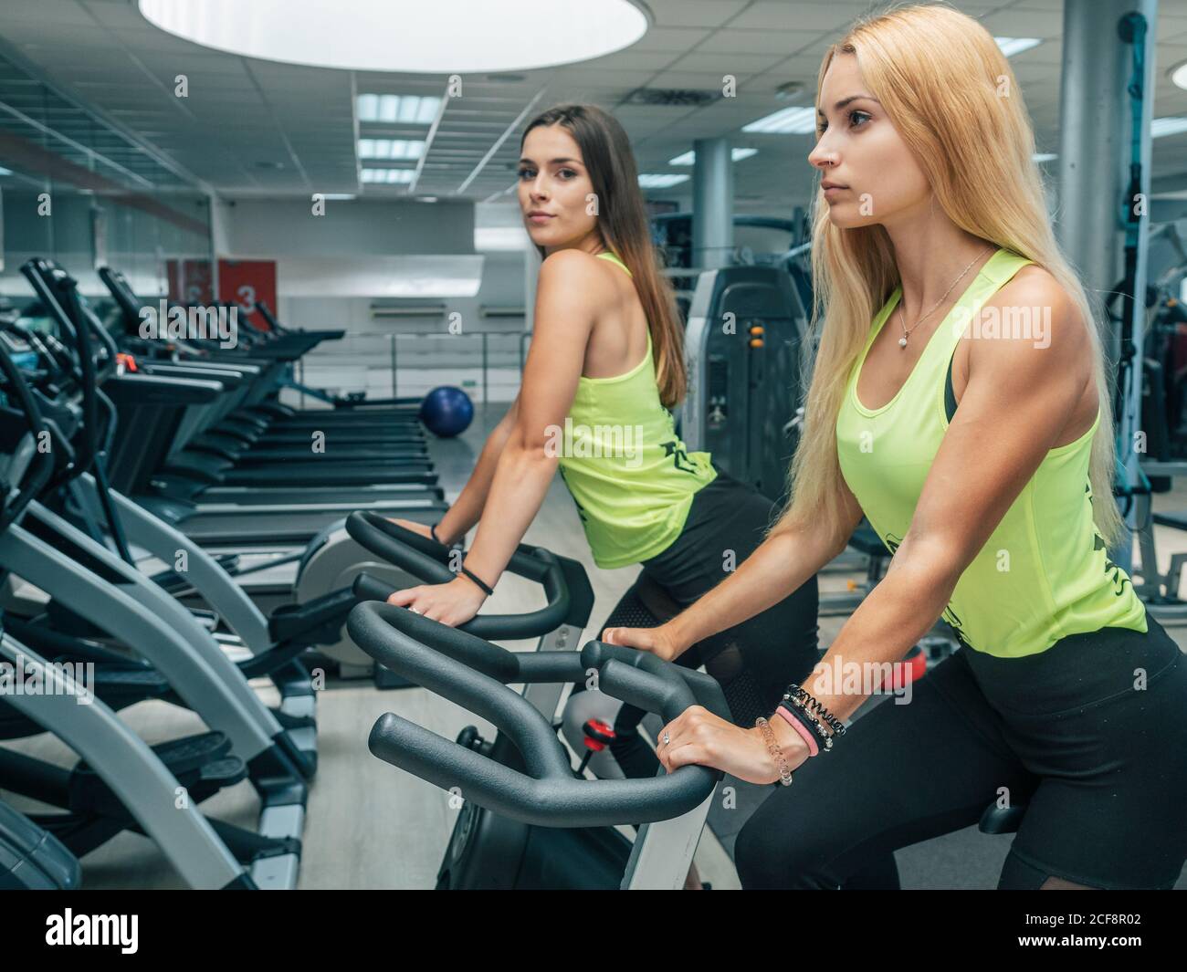 Side view of slim ladies in sportswear training on modern bicycle