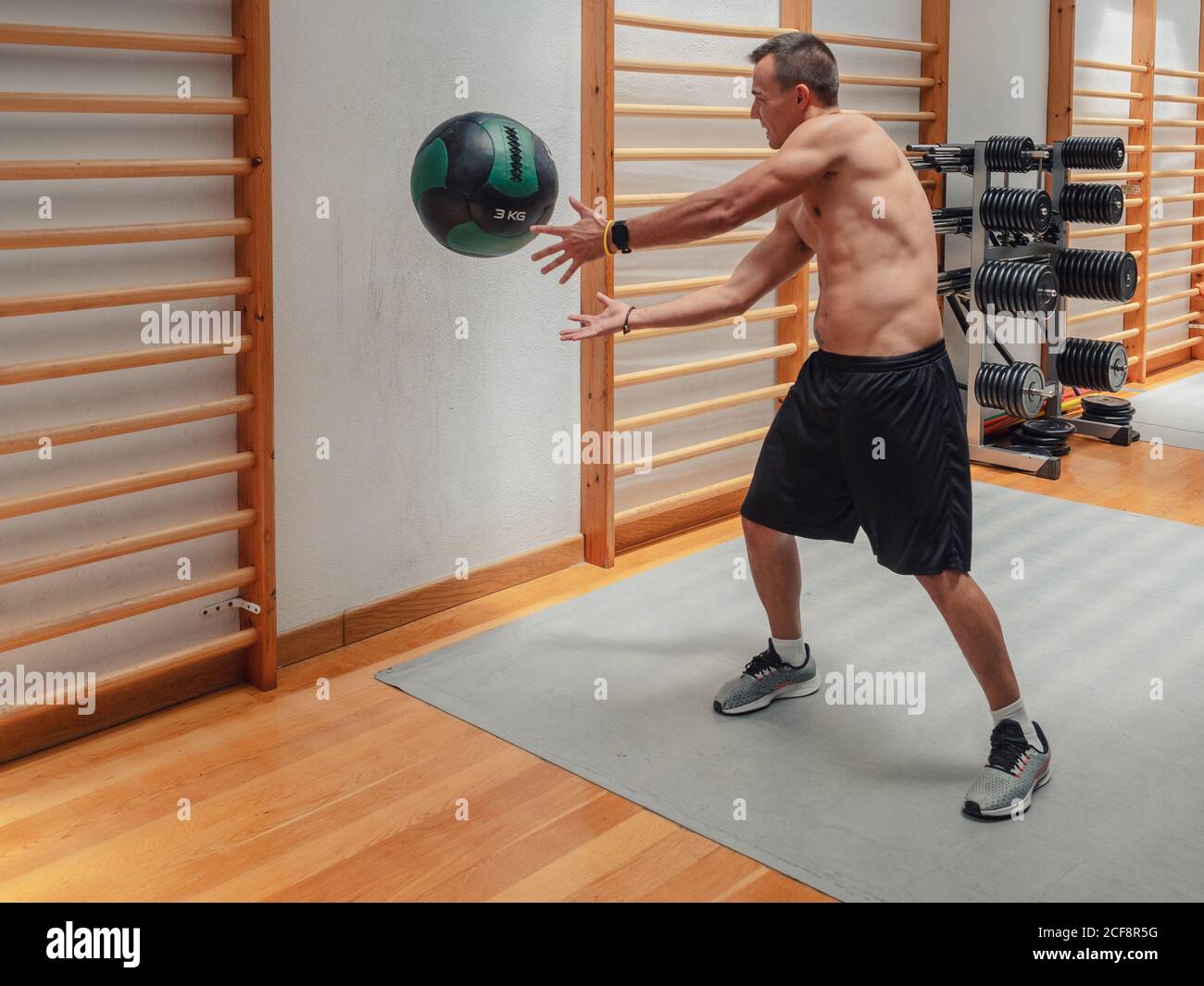 Powerful shirtless male throwing heavy ball against wall during fitness
