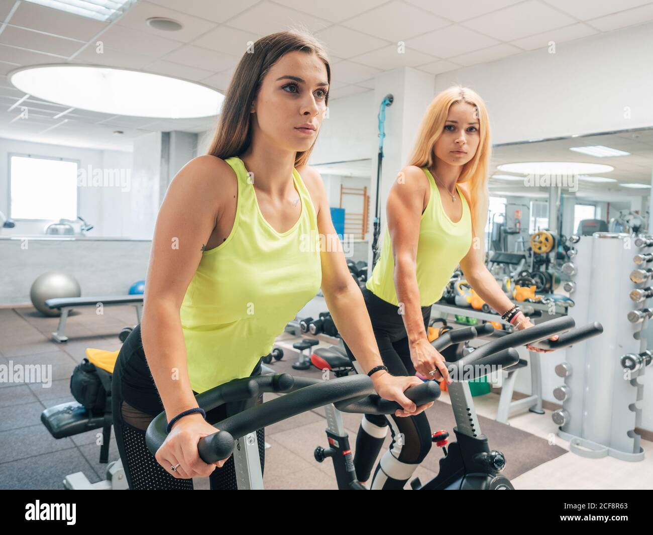 Side view of slim ladies in sportswear training on modern bicycle