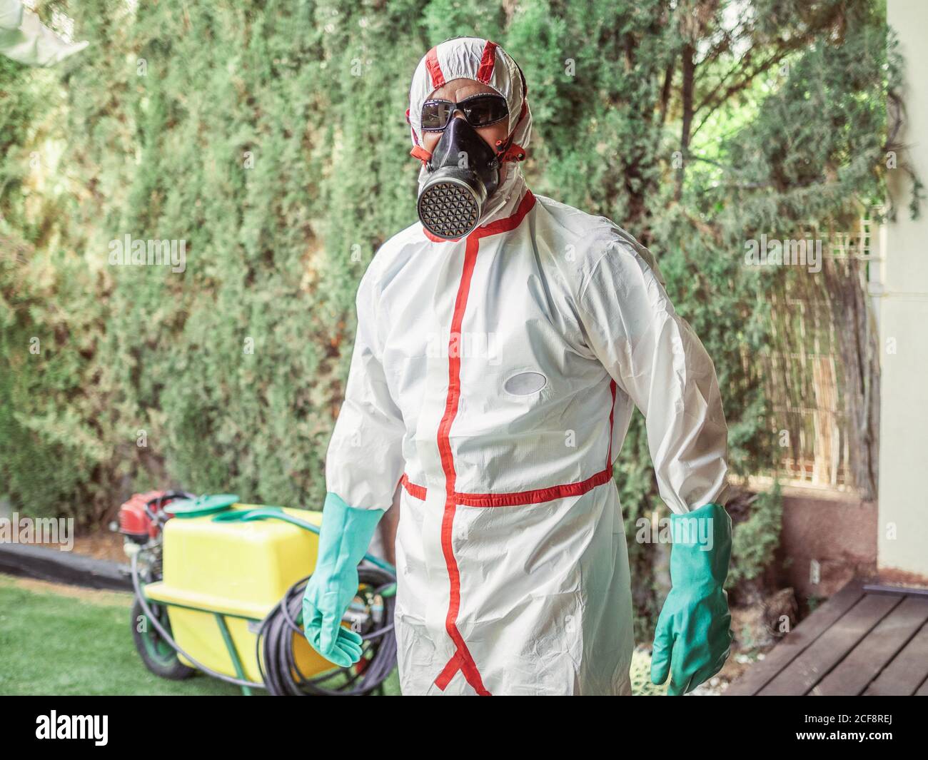 Fumigator in respiratory mask green gloves and white red striped uniform for fumigation ready for disinfection plant in yard Stock Photo