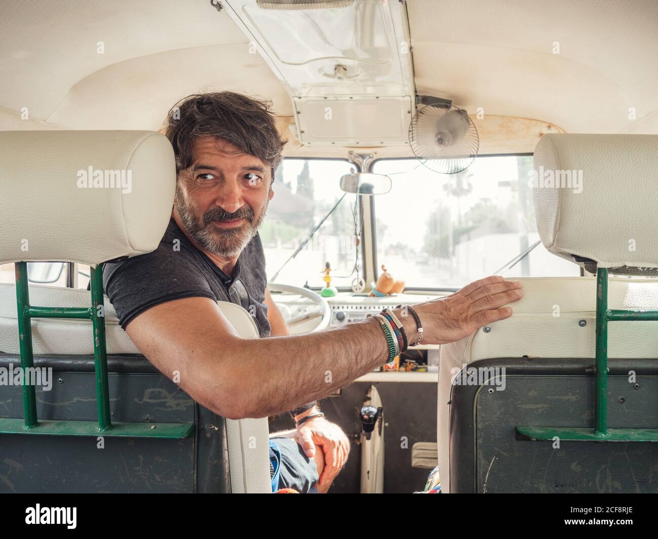 Smiling kind bearded man in front seat watching looking over shoulder in old car Stock Photo