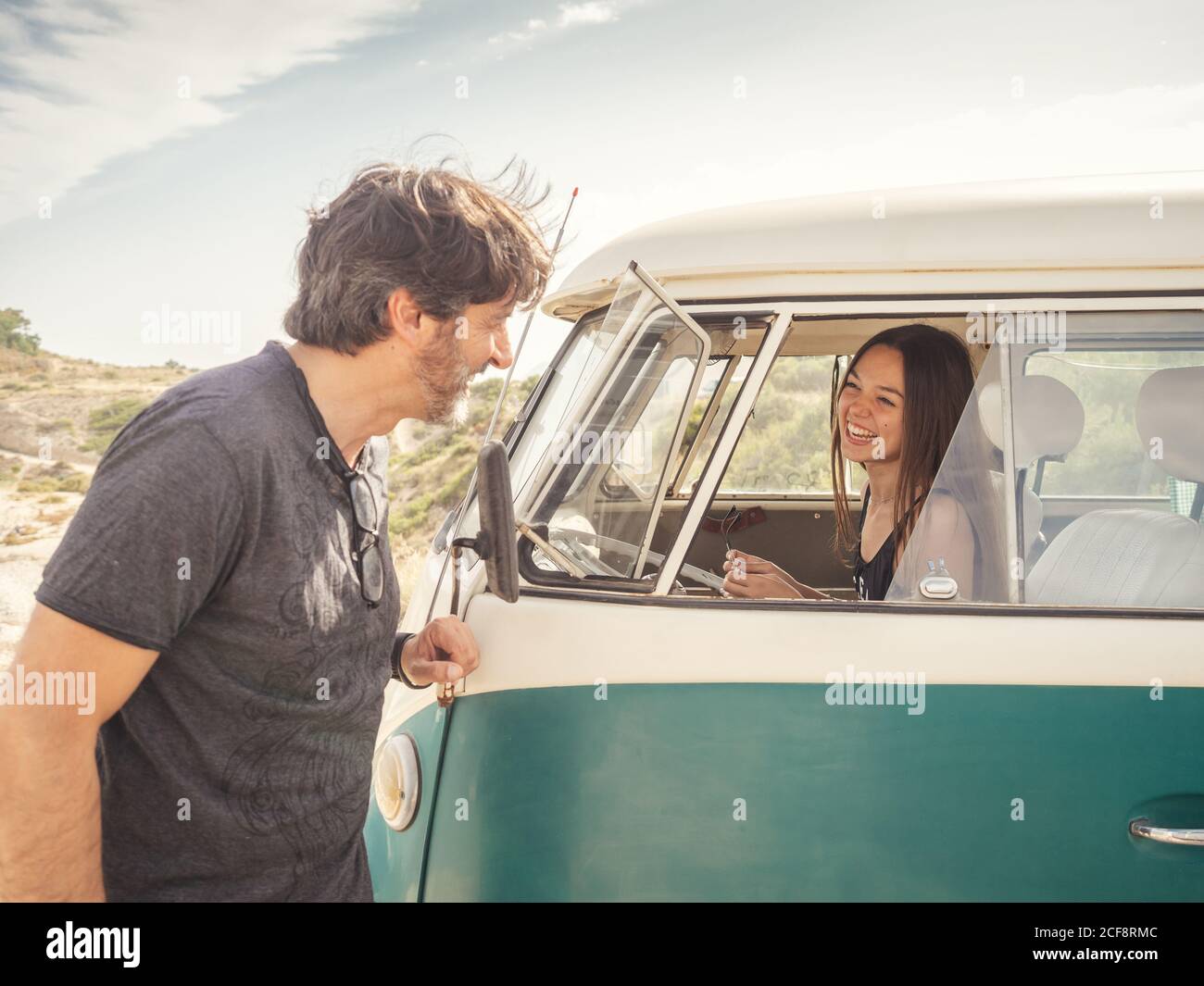Side view of kind smiling man talking to pretty Woman laughing in front seat of car in desert place Stock Photo
