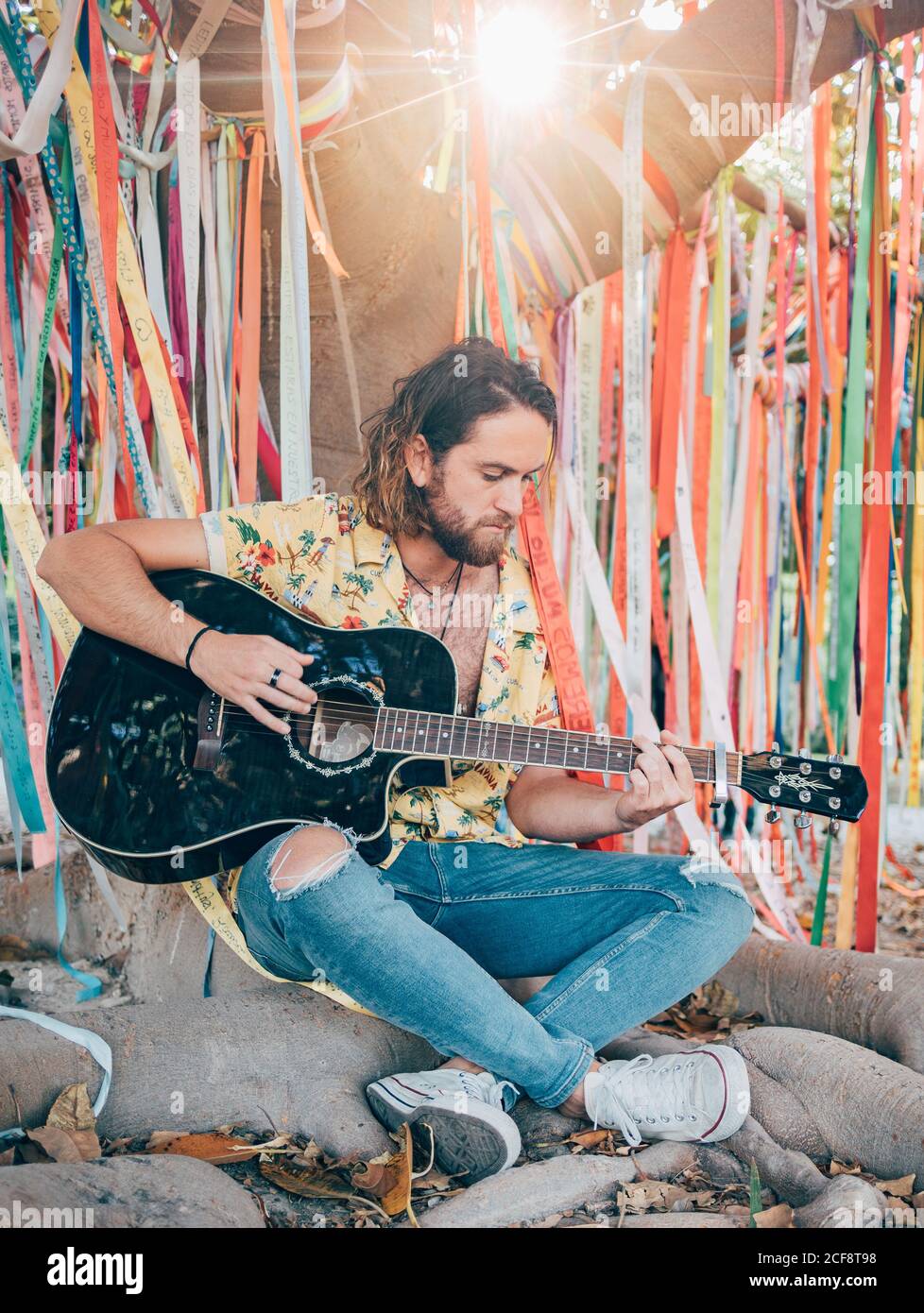 Bearded man sitting under decorated tree playing guitar Stock Photo