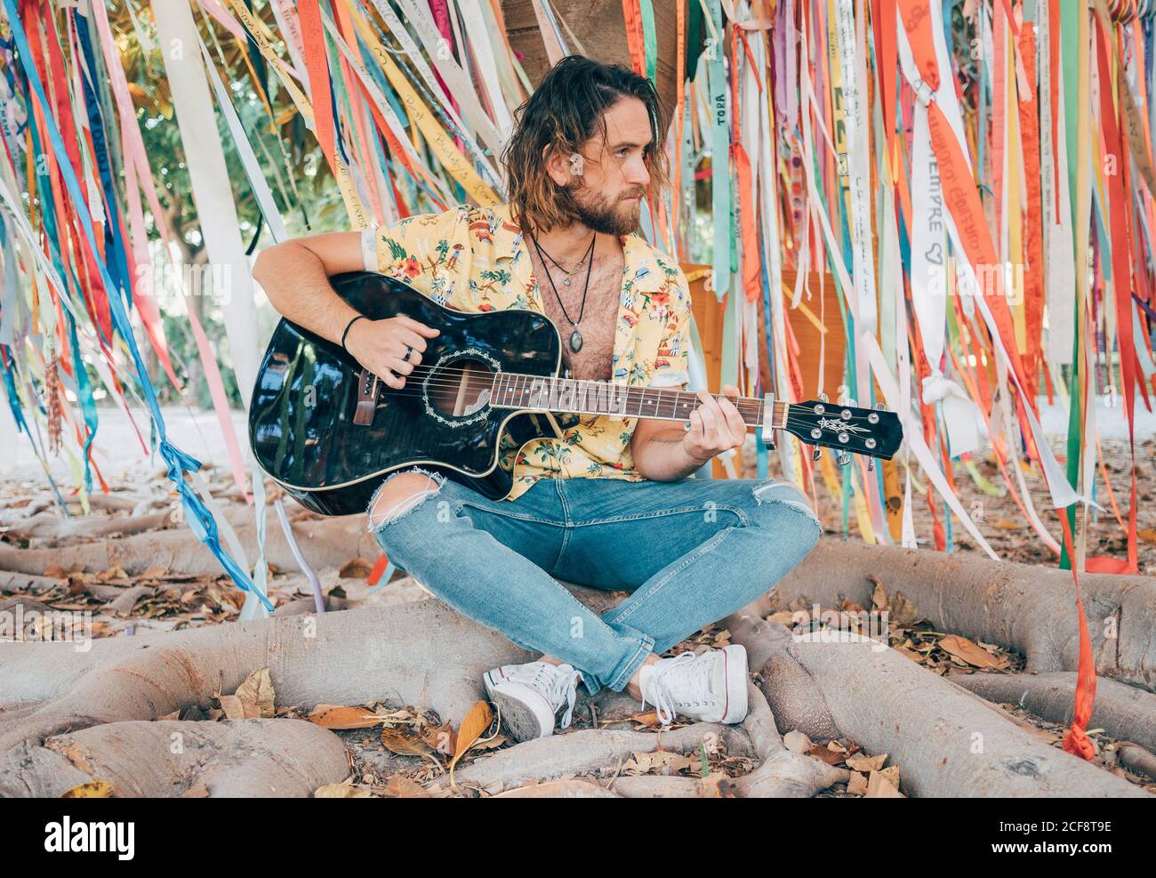 Bearded man sitting under decorated tree playing guitar Stock Photo