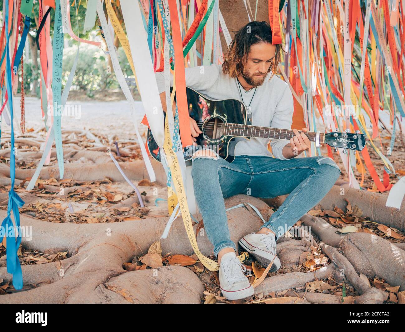 Bearded man sitting under decorated tree playing guitar Stock Photo