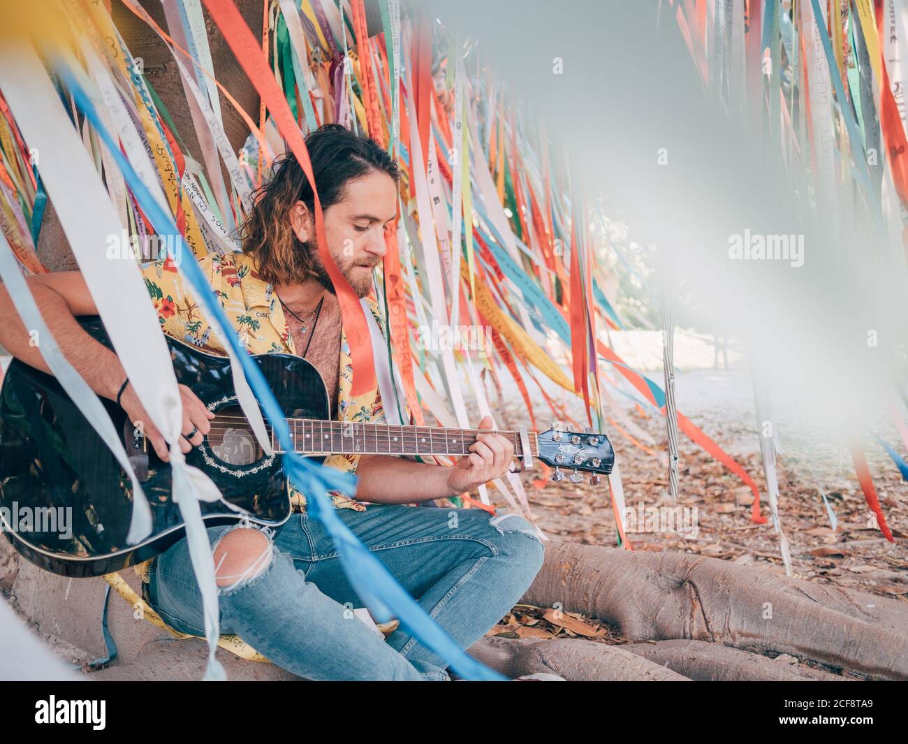 Bearded man sitting under decorated tree playing guitar Stock Photo