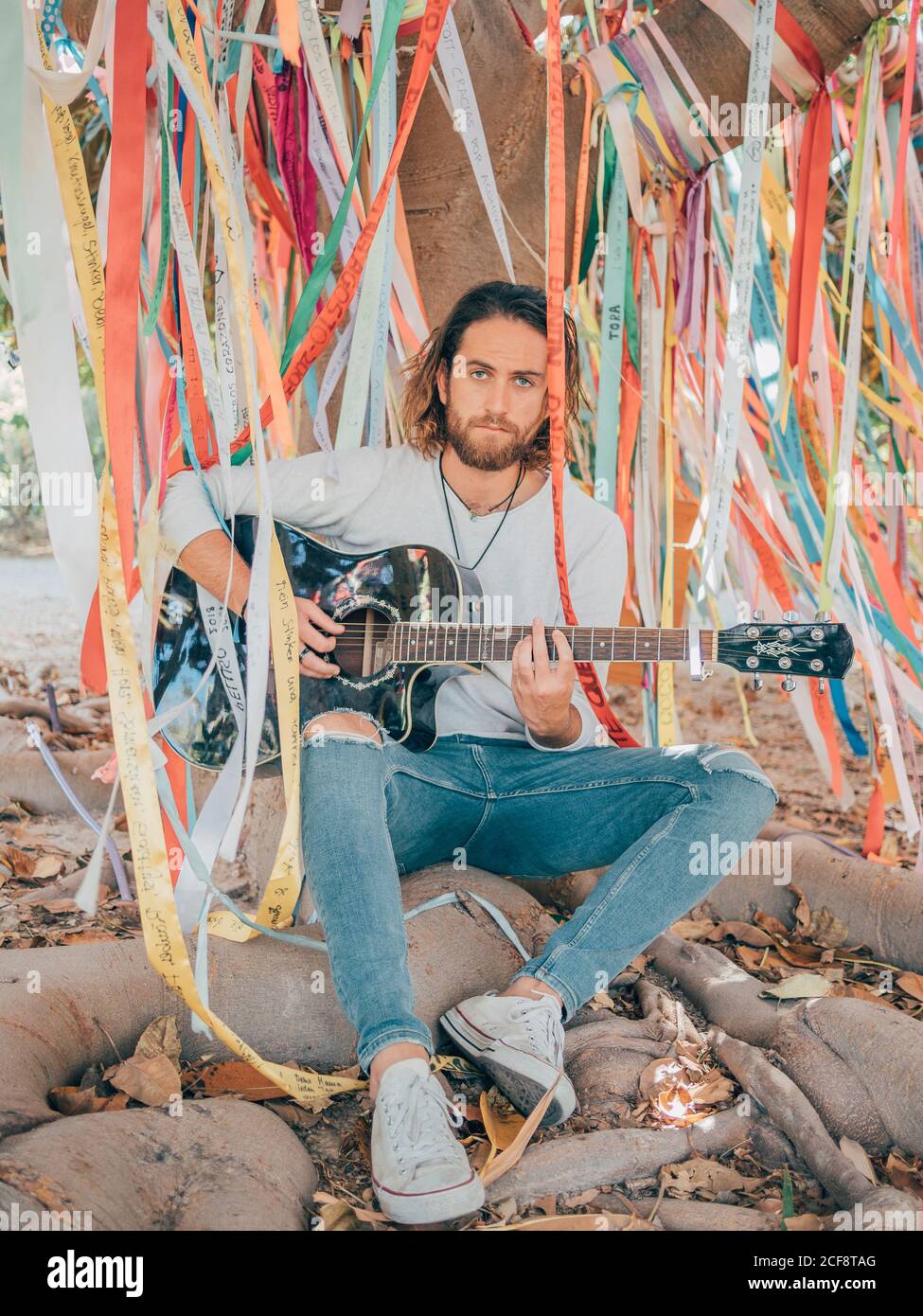 Bearded man sitting under decorated tree playing guitar Stock Photo