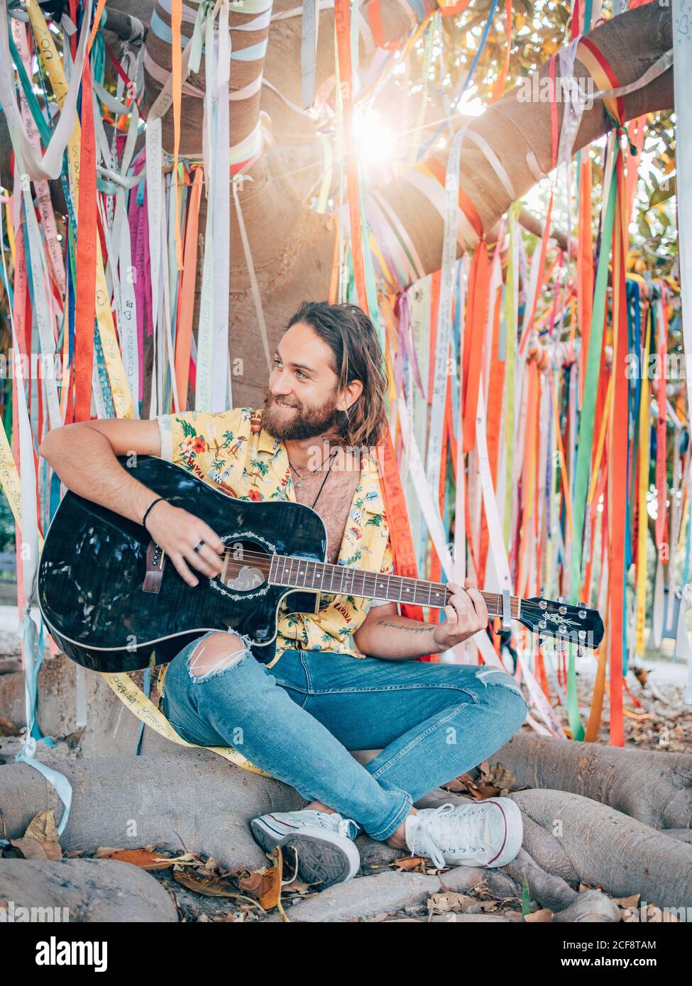 Bearded man sitting under decorated tree playing guitar Stock Photo