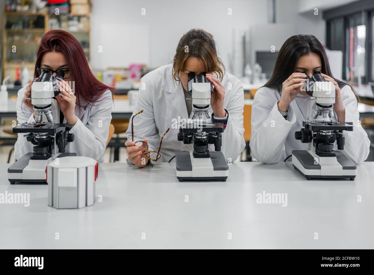 Women in white coats using modern microscopes to examine tissue cells during work in laboratory Stock Photo