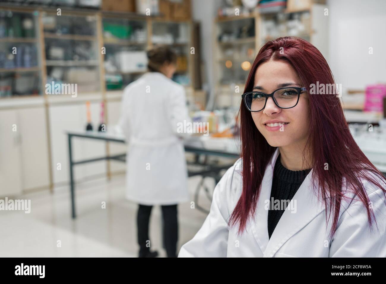 Happy young Woman with red hair smiling and looking at camera while working on scientific research in laboratory in modern university Stock Photo